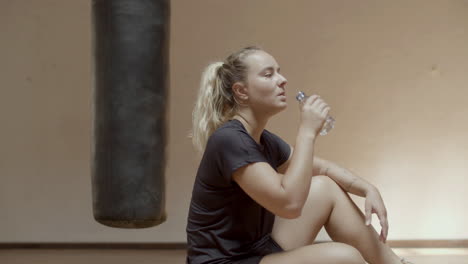 Side-view-of-cute-tired-sportswoman-drinking-water-after-workout